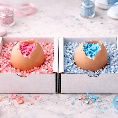 Eggshells with pink and blue contents in a box, surrounded by baby shower decorations.